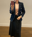 Classic black skirt paired with a pink top and structured blazer. A woman taking a mirror selfie, dressed in a black midi skirt, soft pink top, and dark blazer with gold buttons.