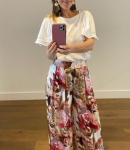 Elegant outfit featuring floral wide-leg pants and a white top. A woman taking a mirror selfie, wearing a white blouse and vibrant floral wide-leg pants in pink and red tones.