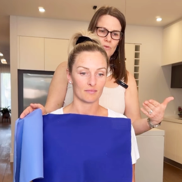 Colour analysis session highlighting best shades with fabric swatches. A personal stylist conducting a colour analysis session with a client, holding blue fabric swatches against the client’s shoulders to determine complementary shades.