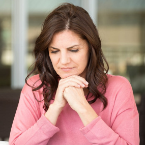 Reflective moment in a pink sweater. A woman in a pink sweater looking pensive, sitting with her hands clasped under her chin.