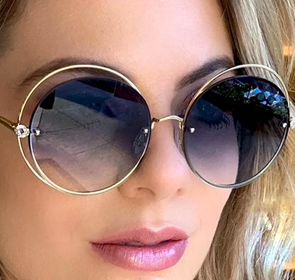 Face-to-Face Eyewear Style Session – Elegant Oversized Sunglasses Selection A close-up of a woman wearing oversized round sunglasses with gold frames and dark gradient lenses. The stylish design features delicate embellishments on the sides, complementing her soft makeup and wavy blonde hair.