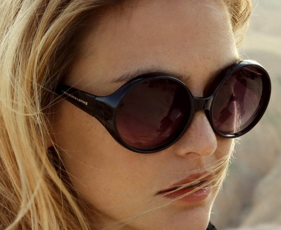 How Eyewear & Glasses Consultation Works – Stylish Oversized Sunglasses Selection A close-up of a woman wearing oversized black round sunglasses with dark lenses. Her blonde hair is tousled by the wind, and the background features a sunlit outdoor setting.