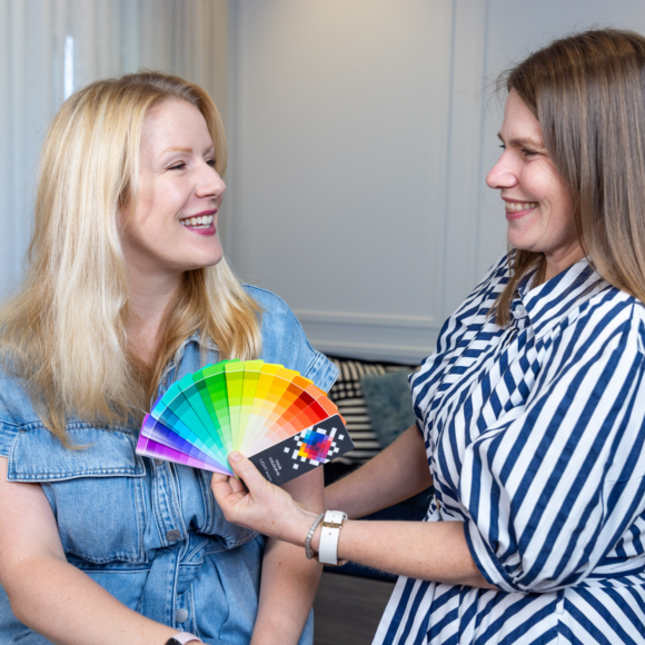 Stylist showing a colour swatch to a smiling blonde woman during a personal colour analysis session