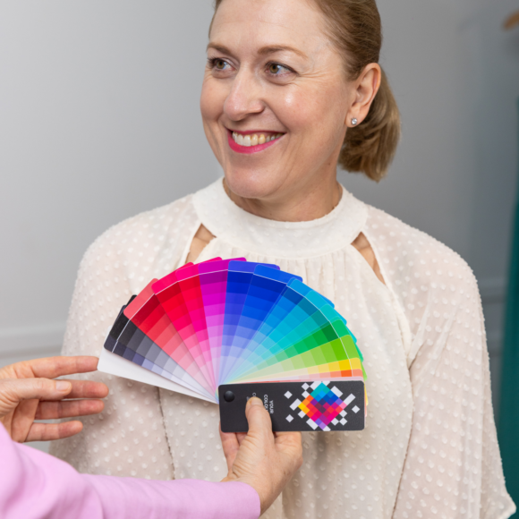 Woman smiling while being shown a vibrant colour swatch fan during a colour analysis session