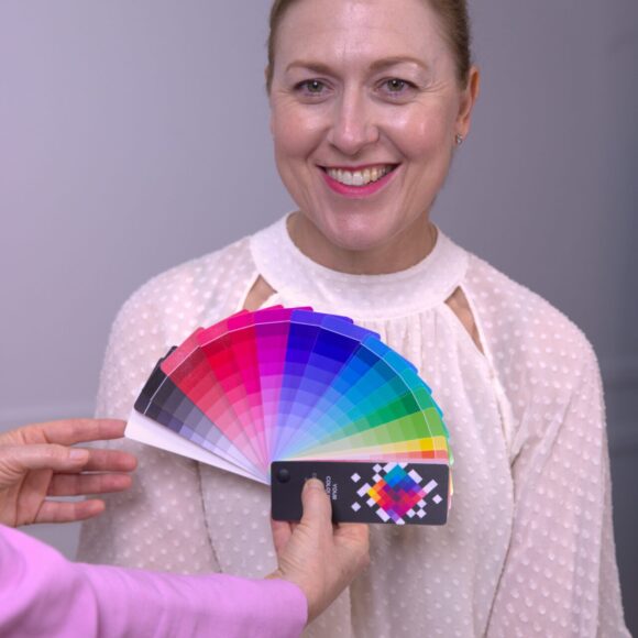 Woman smiling while a stylist presents a colour swatch fan in front of her for colour analysis