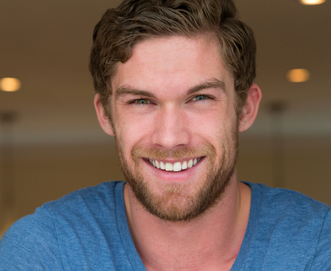 How Hair Style & Colour Consultation Works – Professional Updo Styling in a Salon Smiling young man with short wavy hair and beard, wearing a blue shirt, indoors with soft lighting.